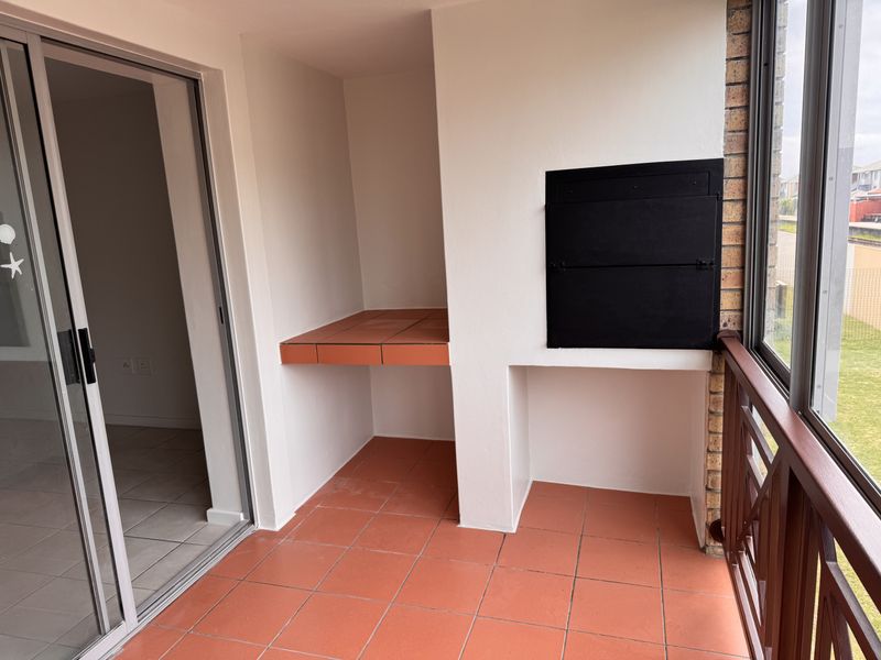 A covered balcony featuring a built-in braai, terracotta-style floor tiles, and a sliding door providing access to the interior living space.