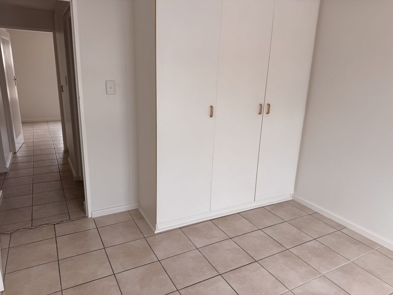 A clean, empty bedroom featuring neutral tiled flooring and white built-in cupboards, offering a versatile space ready for personalization.