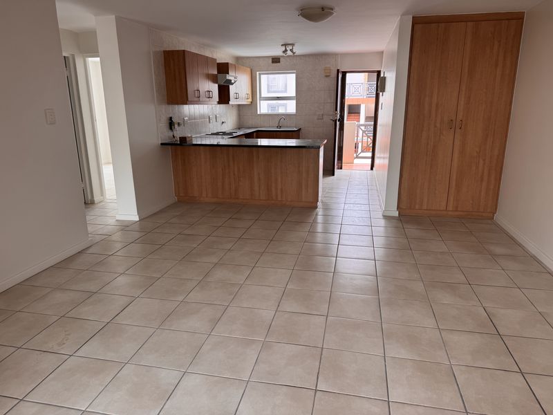 Open plan living and kitchen area featuring tiled flooring, built-in cabinetry with granite countertops, and direct access to an exterior balcony.