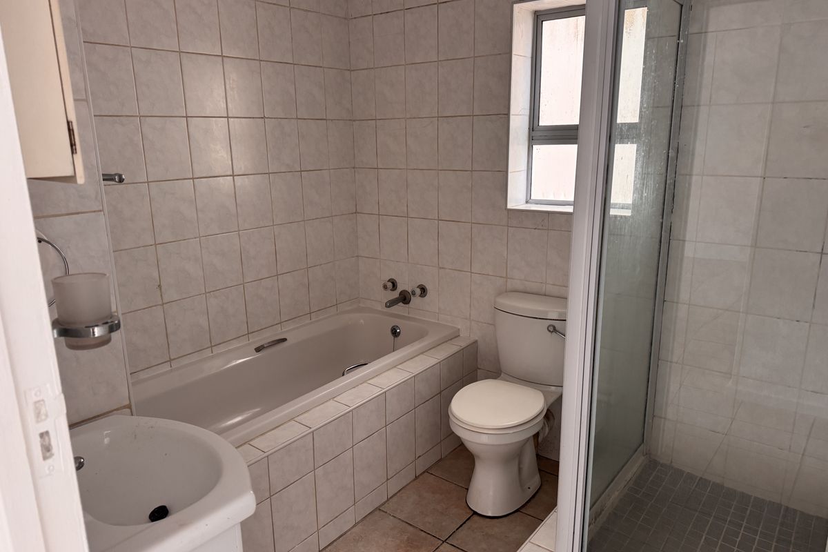 A functional bathroom featuring a built-in bathtub, separate shower enclosure, toilet, and pedestal basin with neutral wall and floor tiling.