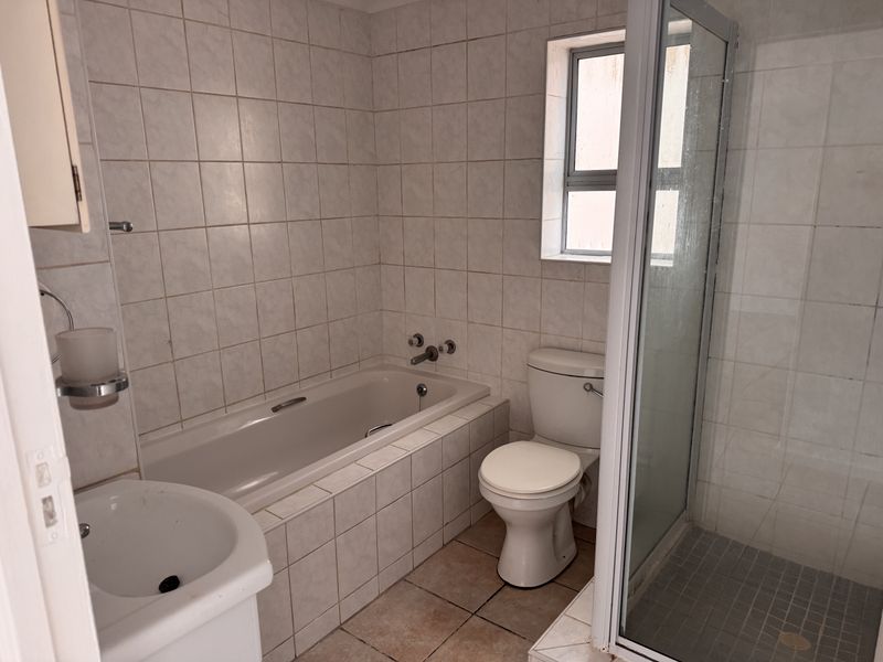A functional bathroom featuring a built-in bathtub, separate shower enclosure, toilet, and pedestal basin with neutral wall and floor tiling.