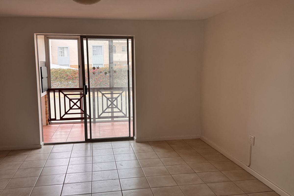 An empty living room featuring neutral ceramic floor tiles and a sliding glass door providing access to an outdoor balcony area.