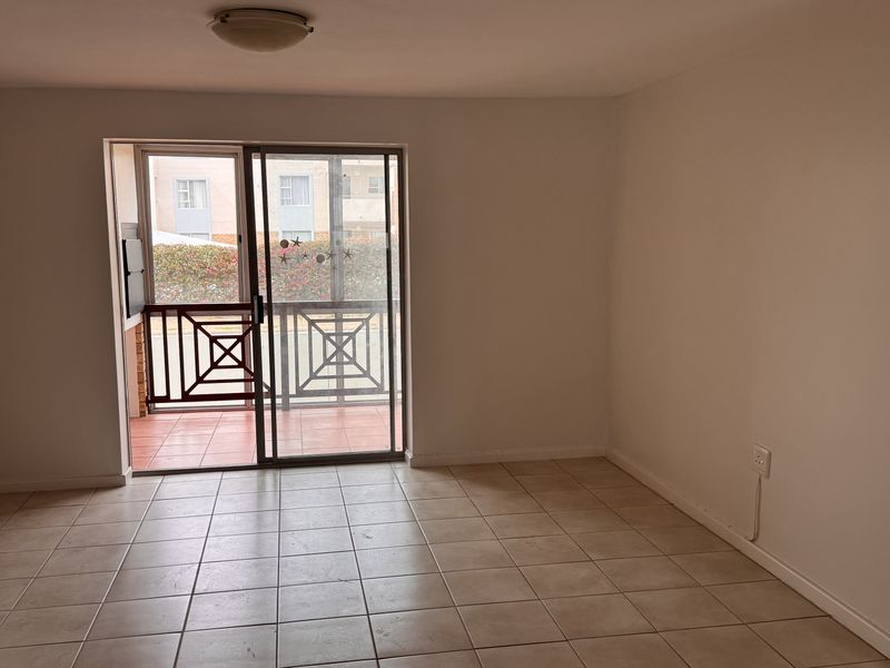 An empty living room featuring neutral ceramic floor tiles and a sliding glass door providing access to an outdoor balcony area.