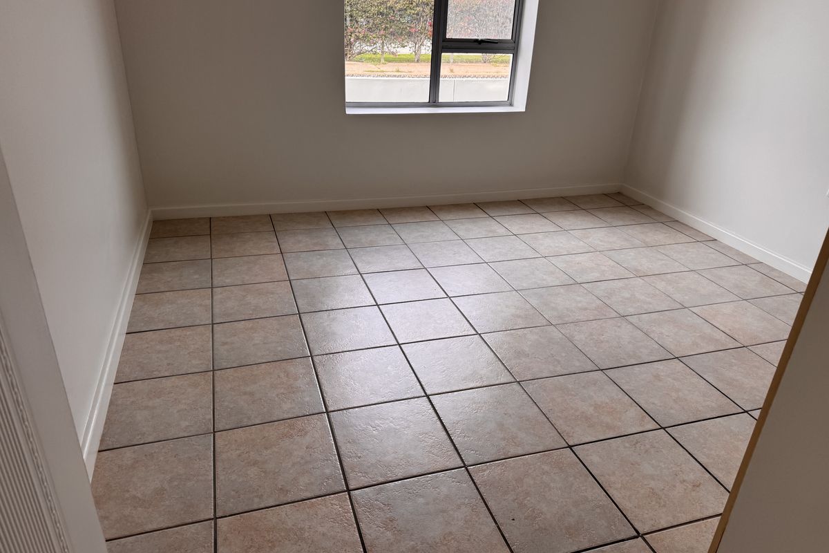 A clean, empty bedroom featuring neutral tiled flooring and a modern aluminium-framed window, providing a blank canvas for interior design.