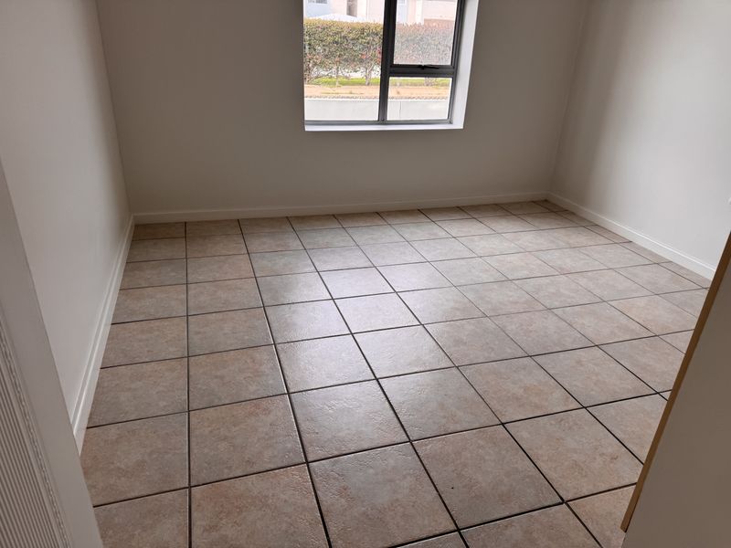 A clean, empty bedroom featuring neutral tiled flooring and a modern aluminium-framed window, providing a blank canvas for interior design.