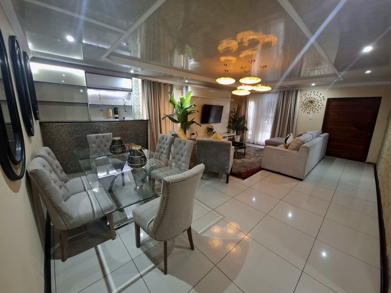Spacious open-plan living and dining area featuring glossy ceilings, tiled flooring, and a built-in bar, creating a modern and cohesive entertainment space.