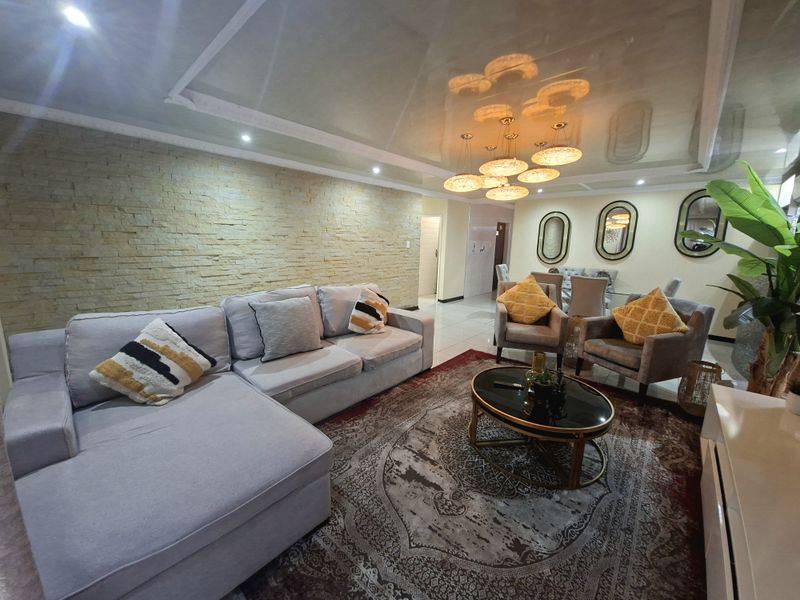 Spacious open-plan living and dining area featuring a striking stacked stone accent wall, glossy ceiling finish, and modern recessed lighting.
