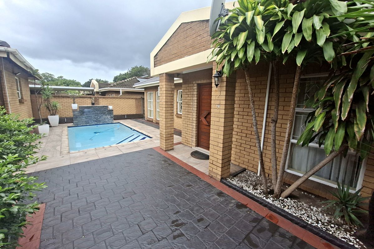 Rear exterior view of a townhouse featuring a private swimming pool, paved patio area, and brick facade construction.