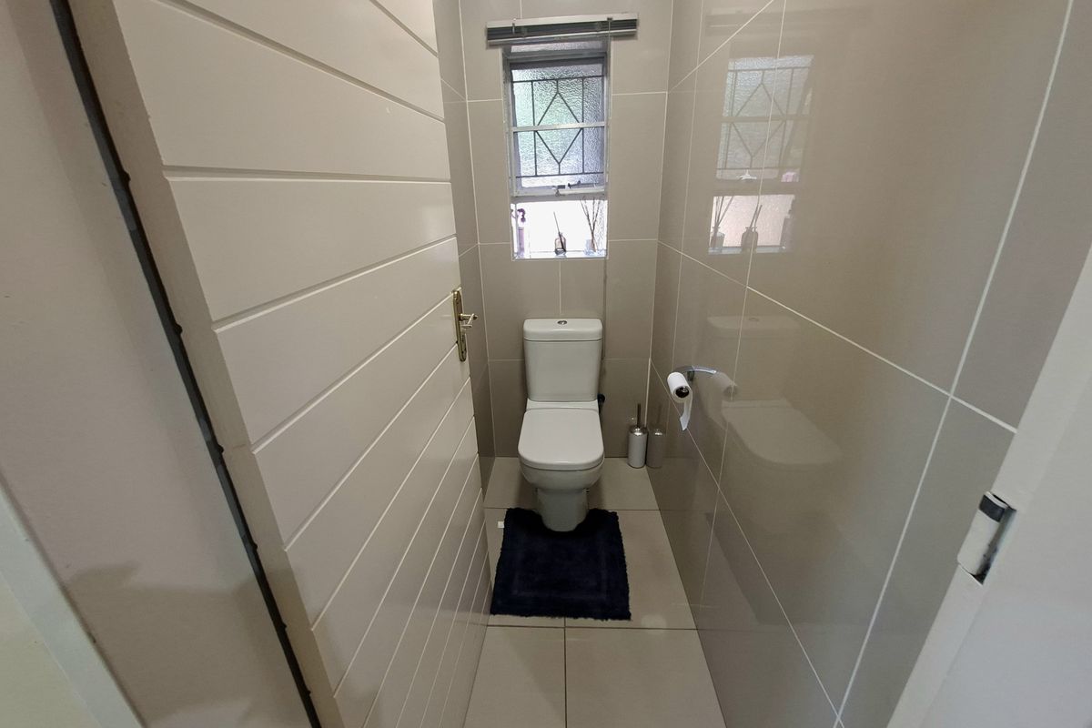 A compact, modern guest bathroom featuring neutral wall and floor tiles, a standard toilet, and a window with security bars.