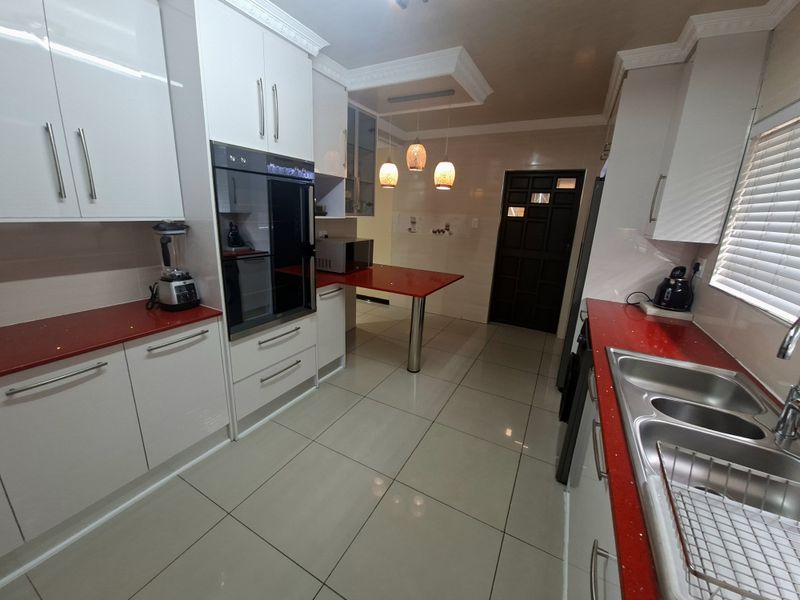 Modern kitchen featuring high-gloss white cabinetry, striking red countertops, built-in oven, breakfast bar, and large format floor tiles.