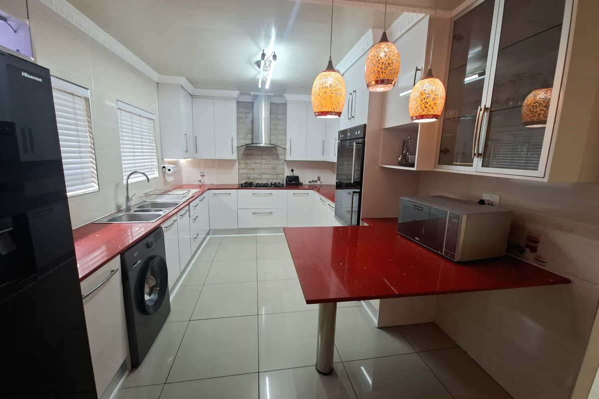 Modern kitchen featuring white cabinetry, striking red stone countertops, built-in oven, stainless steel extractor fan, and tiled flooring with integrated laundry space.