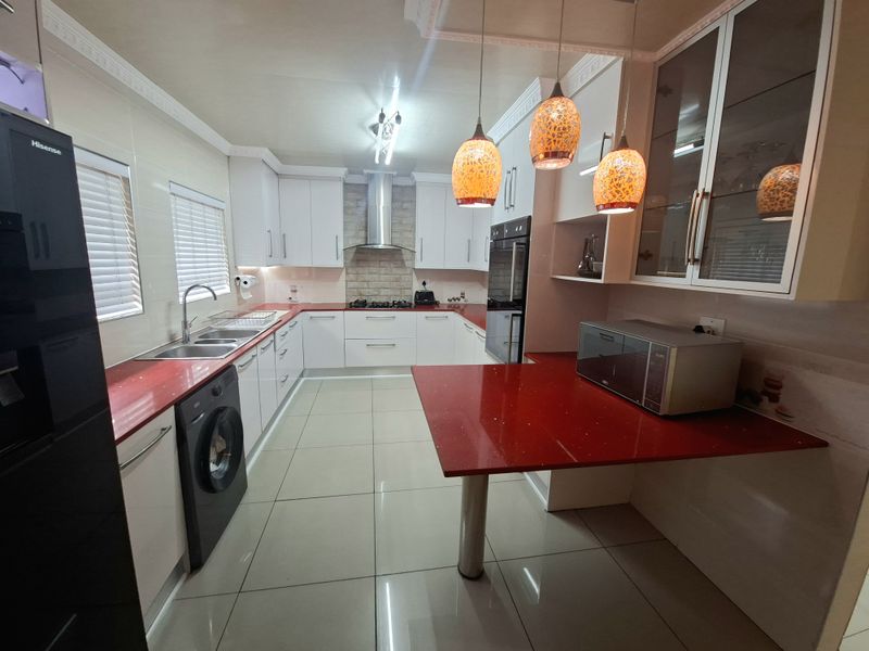 Modern kitchen featuring white cabinetry, striking red stone countertops, built-in oven, stainless steel extractor fan, and tiled flooring with integrated laundry space.