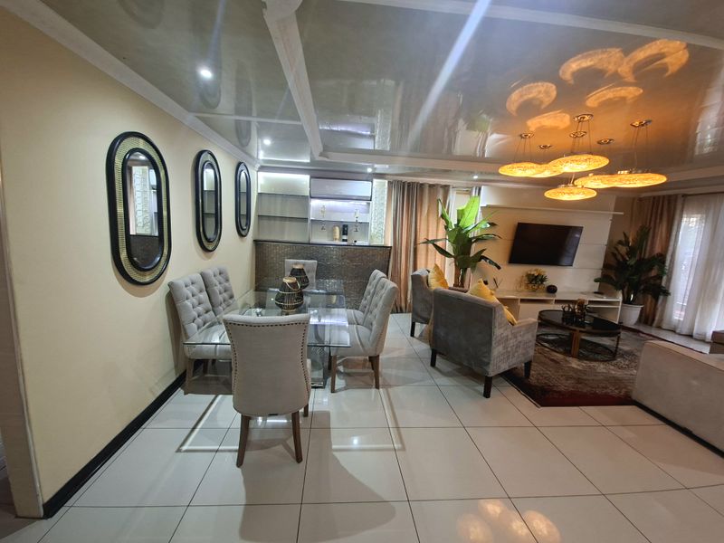 Spacious open-plan living and dining area featuring glossy ceilings, tiled floors, and a built-in bar counter, creating a modern and cohesive entertainment space.