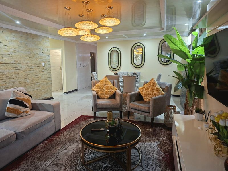 Spacious open-plan living and dining area featuring a stone-clad feature wall, glossy ceiling, and elegant pendant lighting with polished floor tiles throughout.