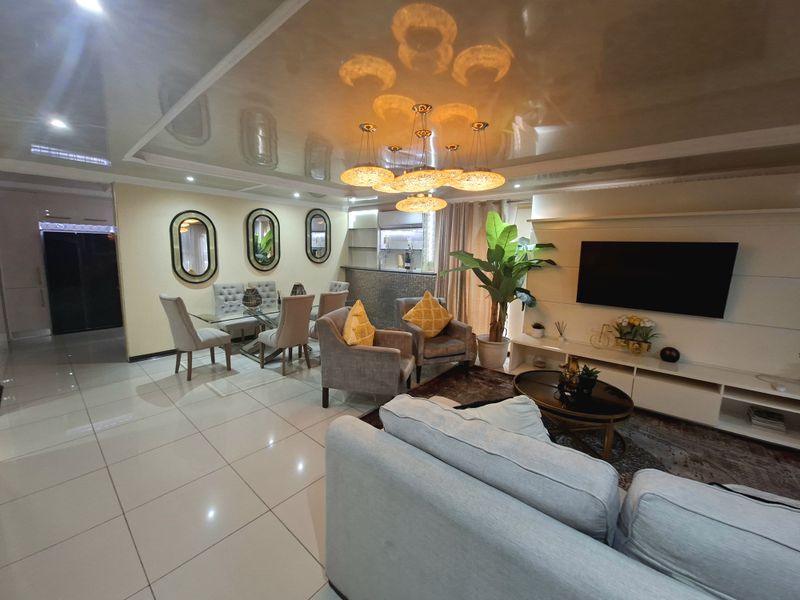 Spacious open-plan living and dining area featuring glossy ceilings, modern tiled flooring, and a built-in media console with an integrated breakfast bar.