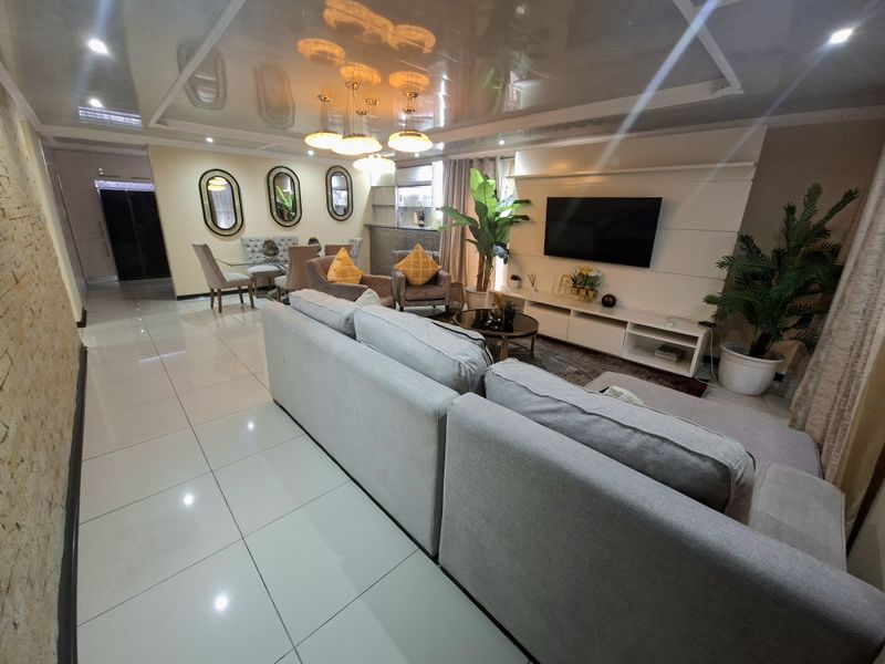 Spacious open-plan living and dining area featuring glossy tiled floors, a modern coffered ceiling with recessed lighting, and a custom built-in media wall.