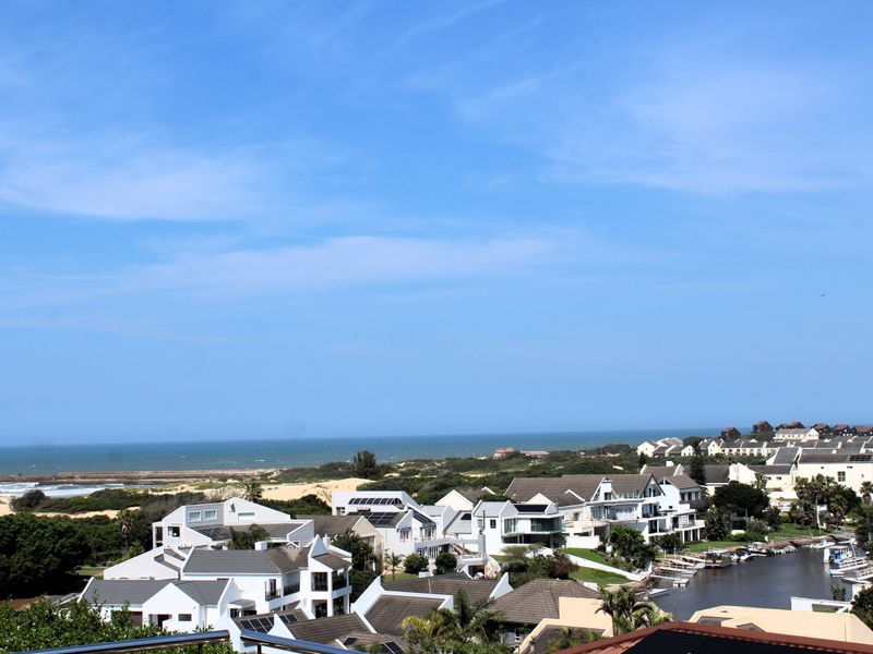 A scenic elevated view overlooking a coastal residential estate, surrounding greenery, and the ocean in the distance.