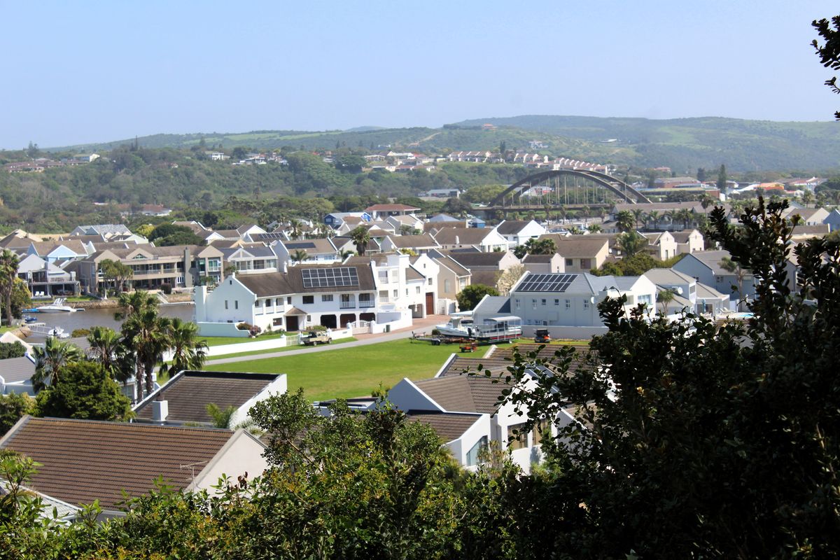 An elevated view overlooking a residential estate with multiple homes, solar panel installations, and a bridge in the background.