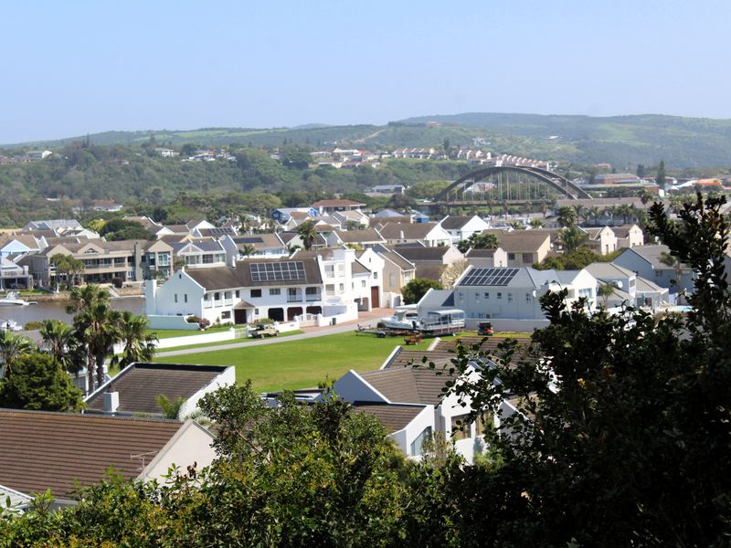 An elevated view overlooking a residential estate with multiple homes, solar panel installations, and a bridge in the background.