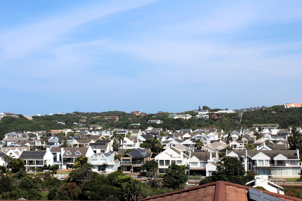 An elevated aerial view of a residential estate featuring numerous homes with tiled roofs, solar installations, and surrounding greenery.