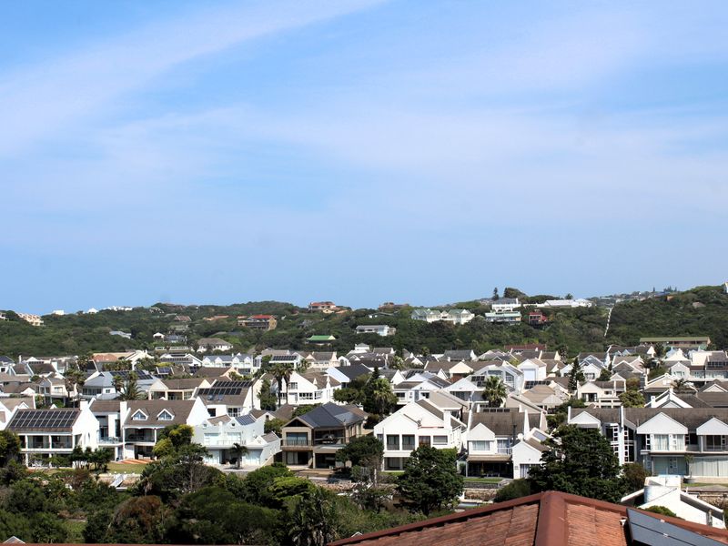 An elevated aerial view of a residential estate featuring numerous homes with tiled roofs, solar installations, and surrounding greenery.