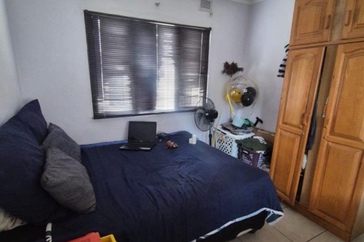 A functional bedroom featuring tiled flooring, a built-in wooden wardrobe, and venetian blinds on the window.