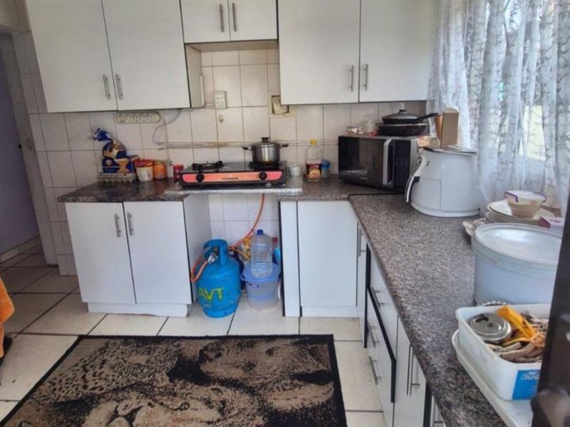 A compact kitchen featuring white cabinetry, laminate countertops, and tiled finishes, requiring some maintenance and cosmetic updates.
