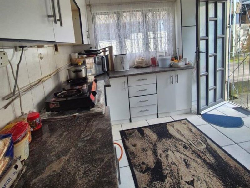 A functional kitchen featuring laminate countertops, built-in cabinetry, and tiled flooring, with direct access to the exterior via a security gate.