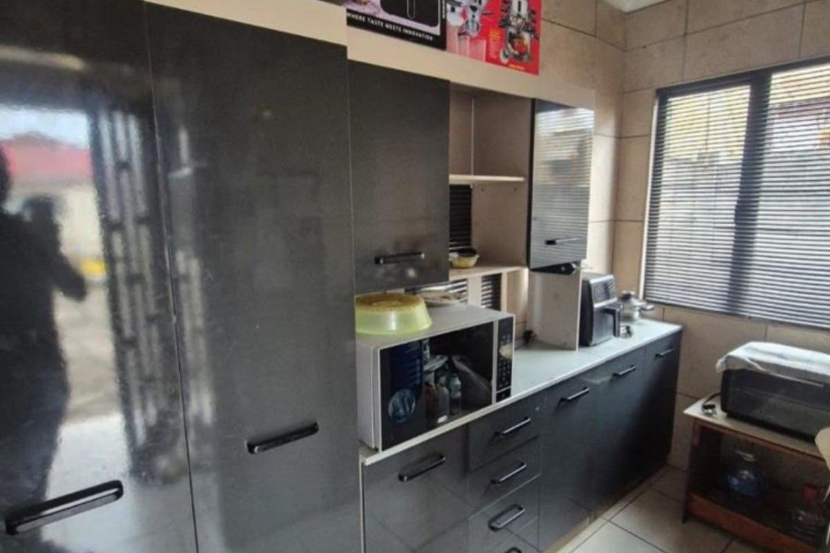 A functional kitchen featuring dark grey built-in cabinetry, tiled flooring, and wall tiling, providing a clean and practical workspace.