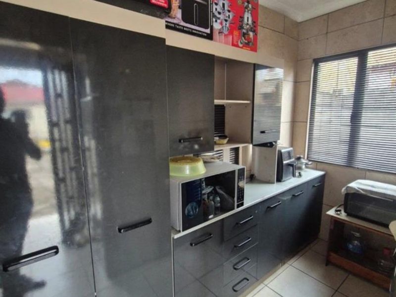 A functional kitchen featuring dark grey built-in cabinetry, tiled flooring, and wall tiling, providing a clean and practical workspace.
