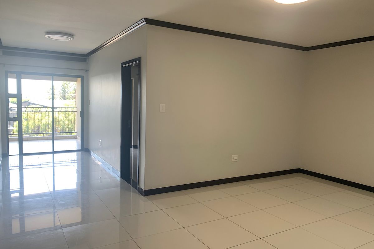 A bright, empty living area featuring polished porcelain floor tiles, dark trim accents, and a sliding glass door leading to an outdoor balcony.