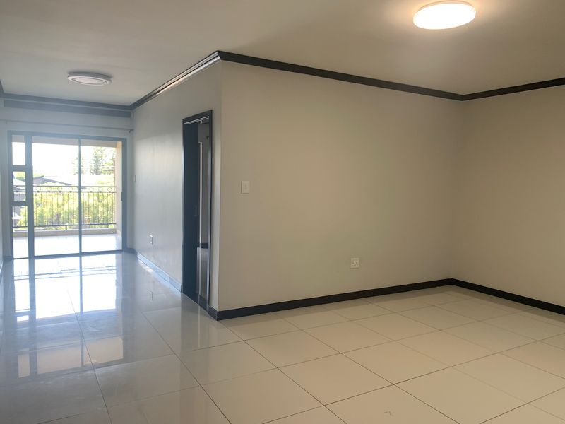 A bright, empty living area featuring polished porcelain floor tiles, dark trim accents, and a sliding glass door leading to an outdoor balcony.