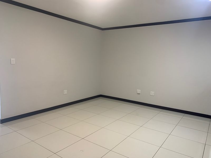 A clean, empty living area featuring neutral wall paint, dark skirting boards, and light-colored floor tiles, providing a versatile blank canvas for interior design.