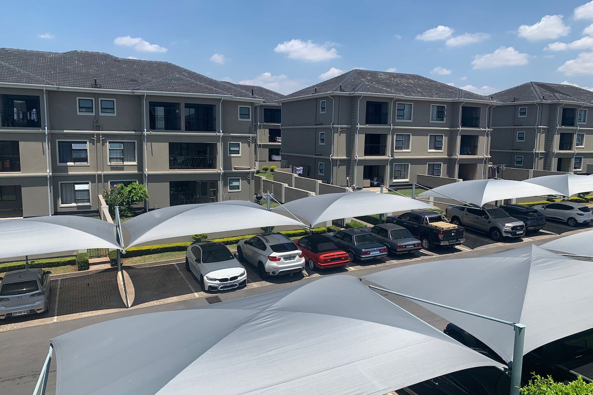 Elevated view of a residential apartment complex featuring multi-story buildings with tiled roofs and dedicated paved parking areas covered by shade cloth structures.