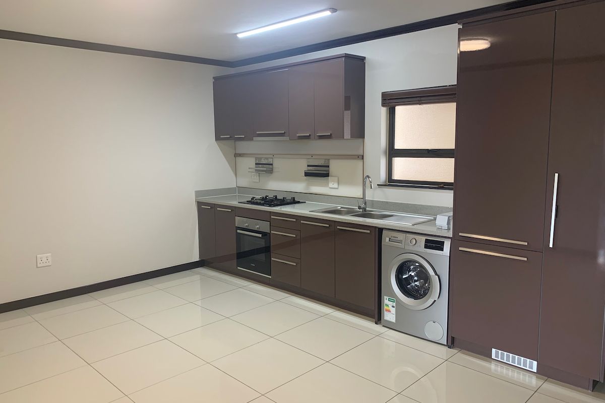 Modern kitchen featuring high-gloss brown cabinetry, gas hob, built-in oven, stainless steel sink, and tiled flooring in a clean, open-plan layout.