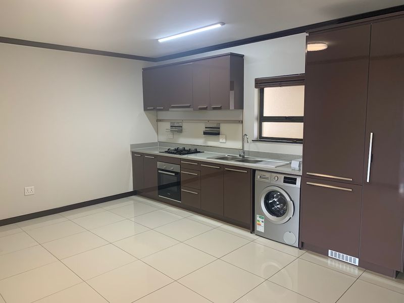 Modern kitchen featuring high-gloss brown cabinetry, gas hob, built-in oven, stainless steel sink, and tiled flooring in a clean, open-plan layout.