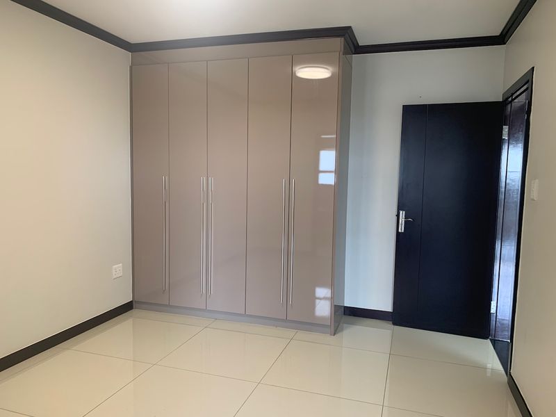A clean, modern bedroom featuring high-gloss built-in cupboards, neutral tiled flooring, and dark contrasting trim details.