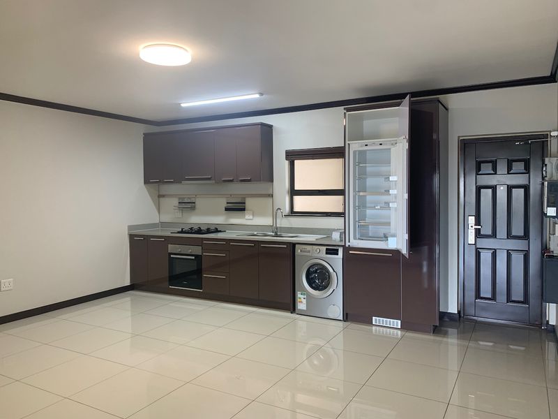 Modern open-plan kitchen featuring dark cabinetry, integrated appliances, gas hob, electric oven, and tiled flooring, adjacent to the main entrance door.