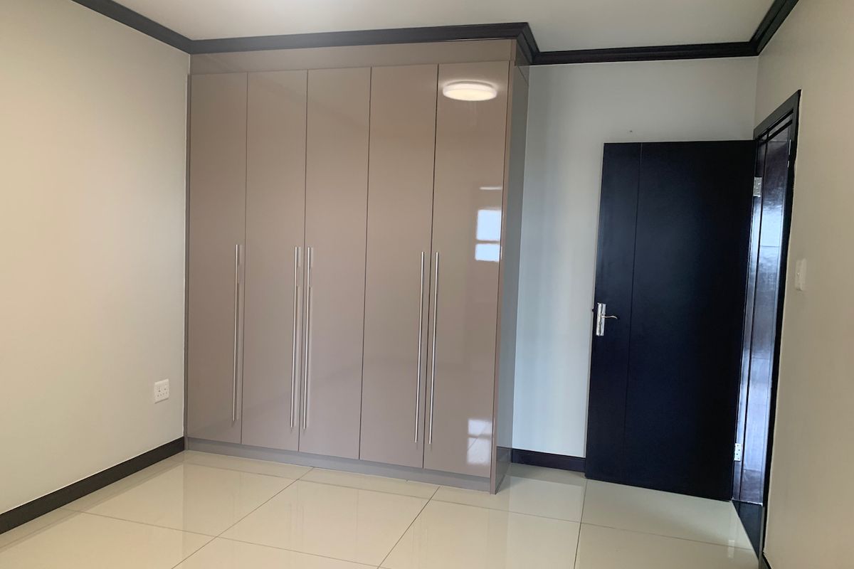 A clean, empty bedroom featuring modern high-gloss built-in cupboards, neutral tiled flooring, and dark contrasting door and trim finishes.