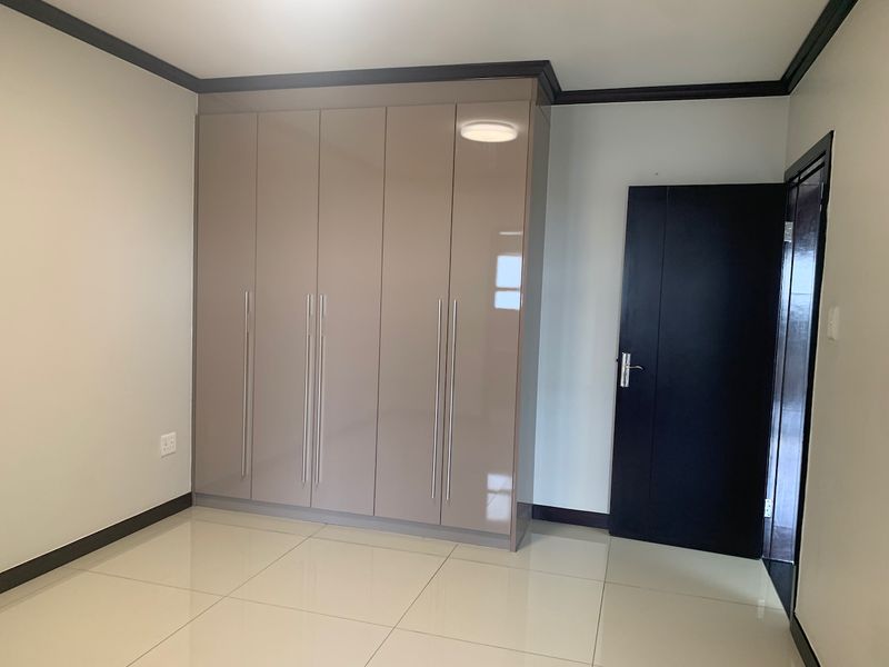 A clean, empty bedroom featuring modern high-gloss built-in cupboards, neutral tiled flooring, and dark contrasting door and trim finishes.