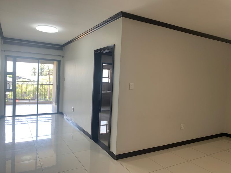 An empty, well-maintained living area featuring polished tiled floors, dark trim accents, and a sliding glass door providing access to an outdoor balcony.