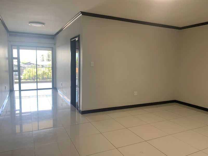 A bright, empty living area featuring neutral tiled flooring, dark trim accents, and a sliding glass door leading to an outdoor balcony.