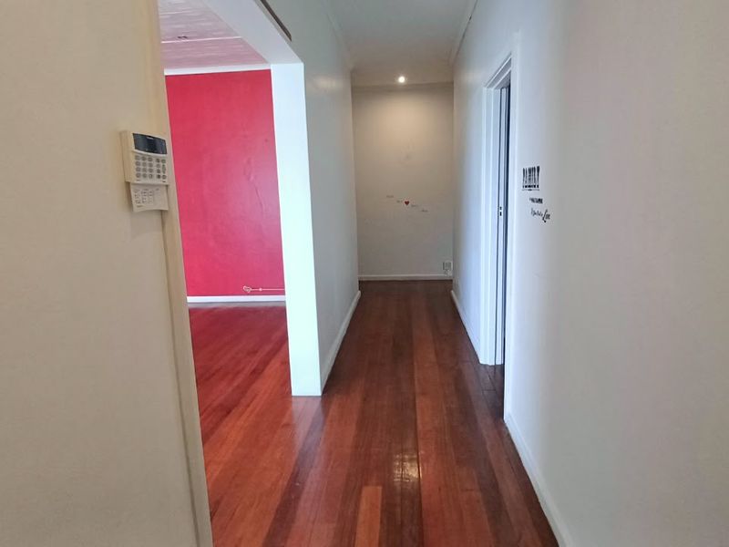 A bright, empty hallway featuring polished hardwood flooring and an integrated alarm system keypad, leading into an adjacent living area.