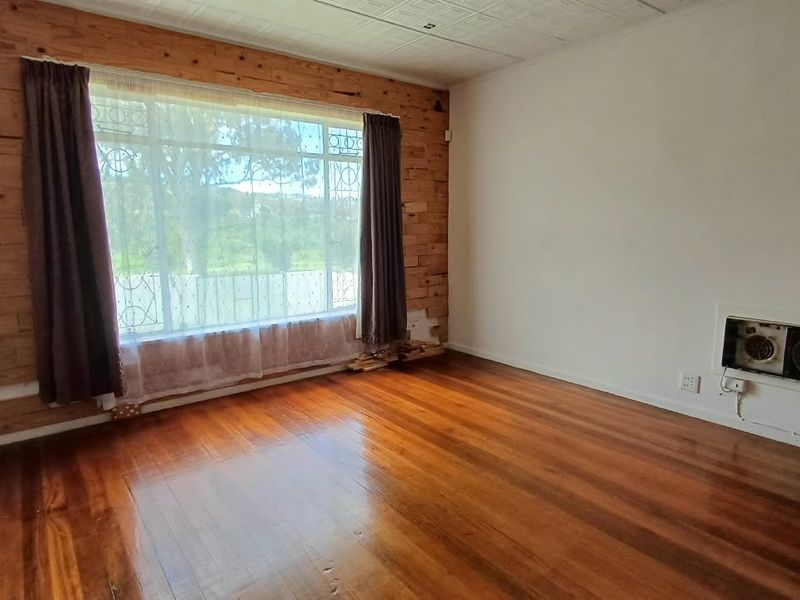 An empty living room featuring polished timber flooring, a feature timber-clad wall, and a built-in wall heater.
