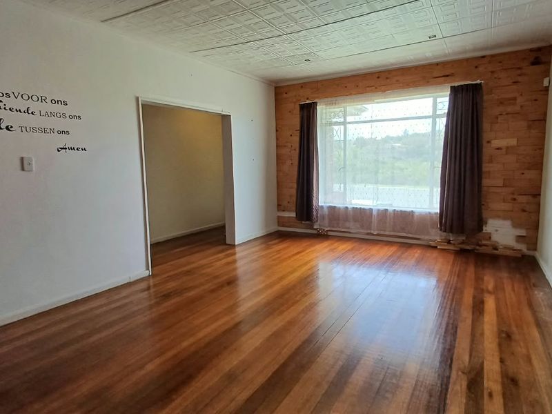 Spacious living room featuring polished hardwood floors, a unique pressed metal ceiling, and a feature timber-clad wall with large window for natural light.