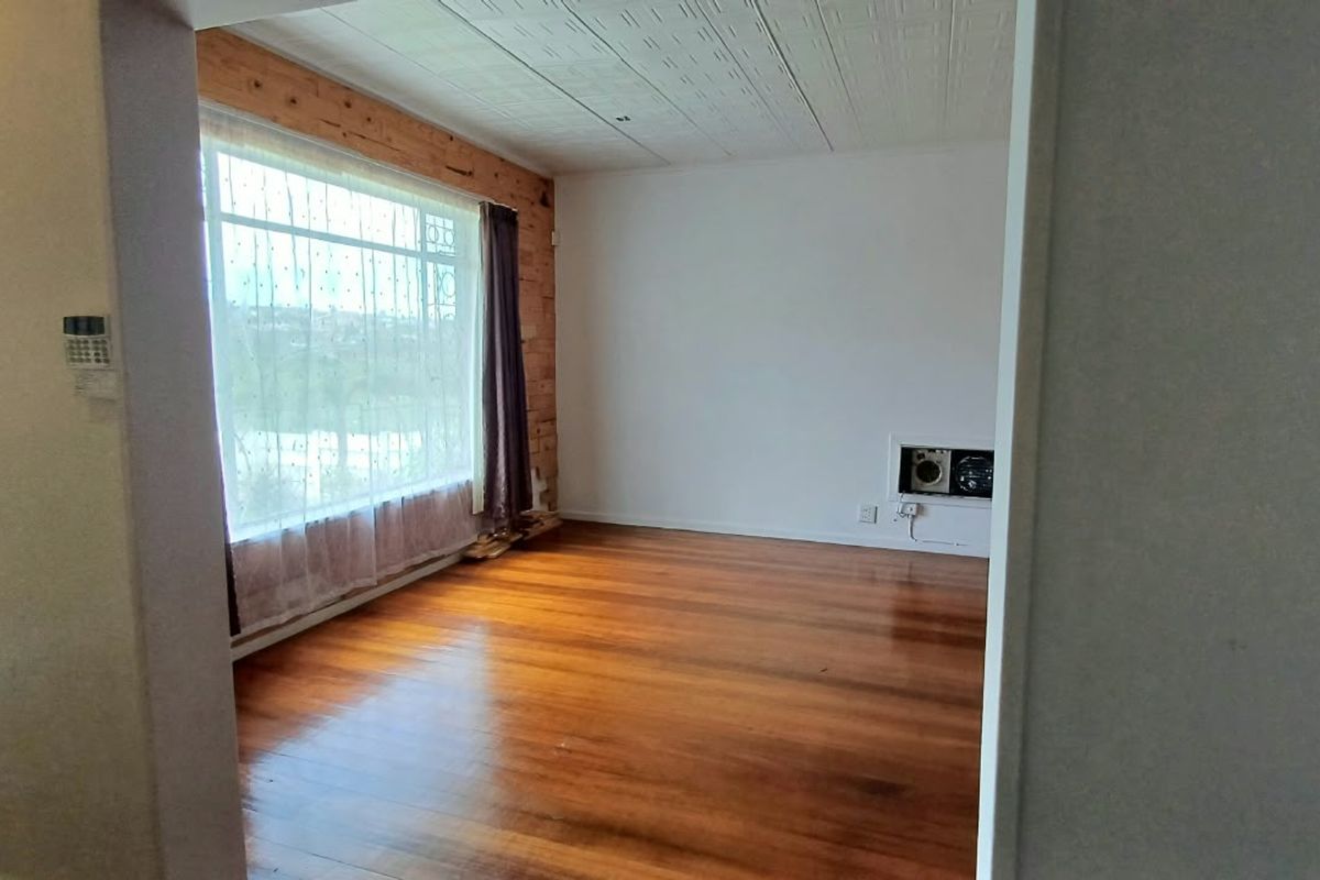 An empty living room featuring polished hardwood floors, a large window with natural light, and unique timber wall detailing.