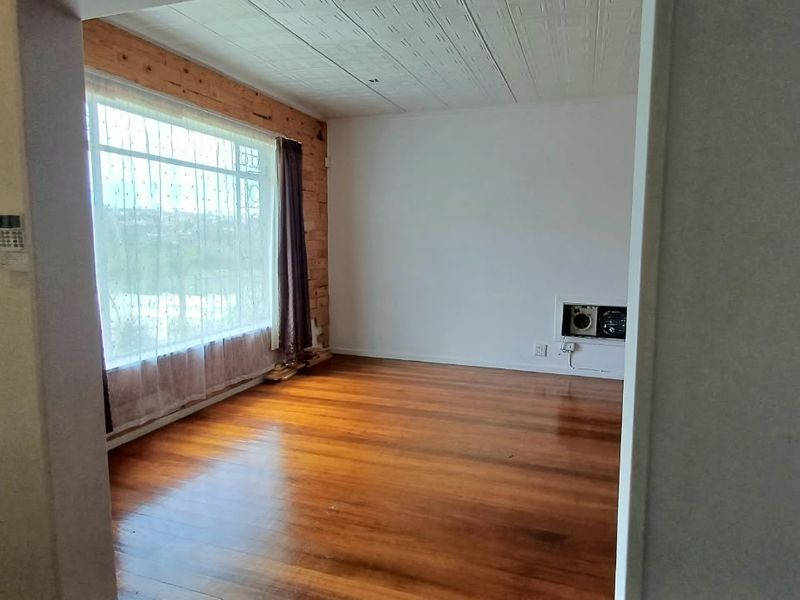 An empty living room featuring polished hardwood floors, a large window with natural light, and unique timber wall detailing.