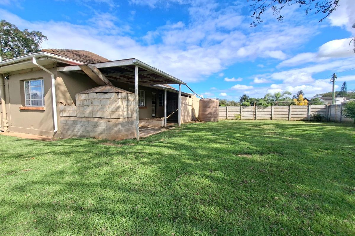 Rear view of the property featuring a spacious lawn, a covered patio area with a built-in braai, and a water storage tank.
