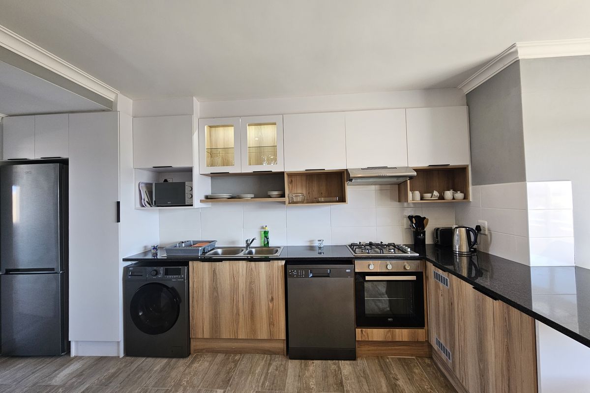 Modern kitchen featuring wood-grain cabinetry, granite countertops, built-in oven, gas hob, extractor fan, and integrated storage solutions.