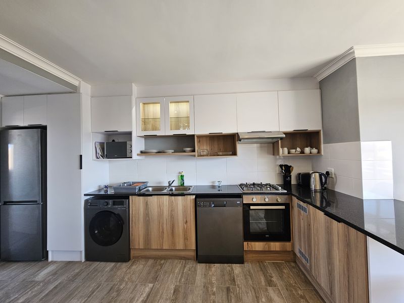 Modern kitchen featuring wood-grain cabinetry, granite countertops, built-in oven, gas hob, extractor fan, and integrated storage solutions.